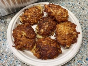 A white plate topped with six cooked latkes.
